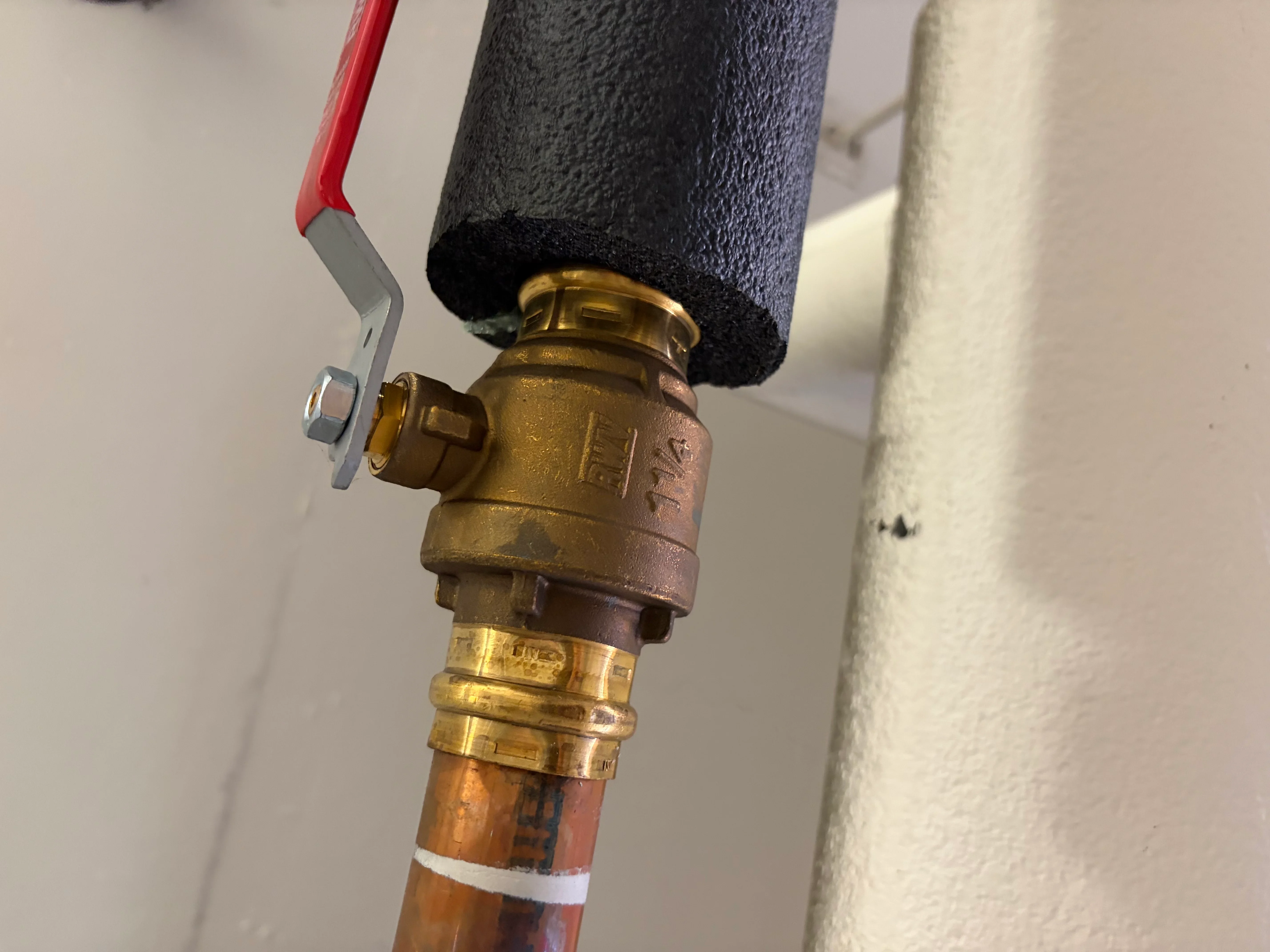 Brass ball valve with red handle installed on copper pipe with foam insulation wrap