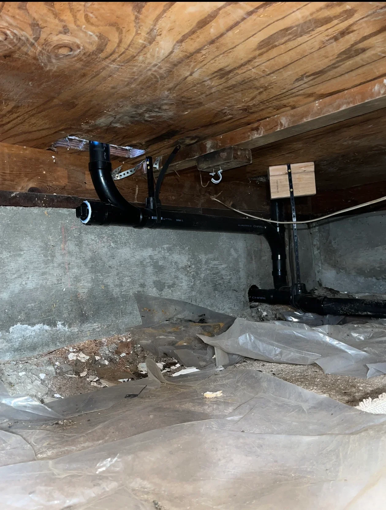 Sump pump installation in crawl space with black discharge pipe and plastic vapor barrier