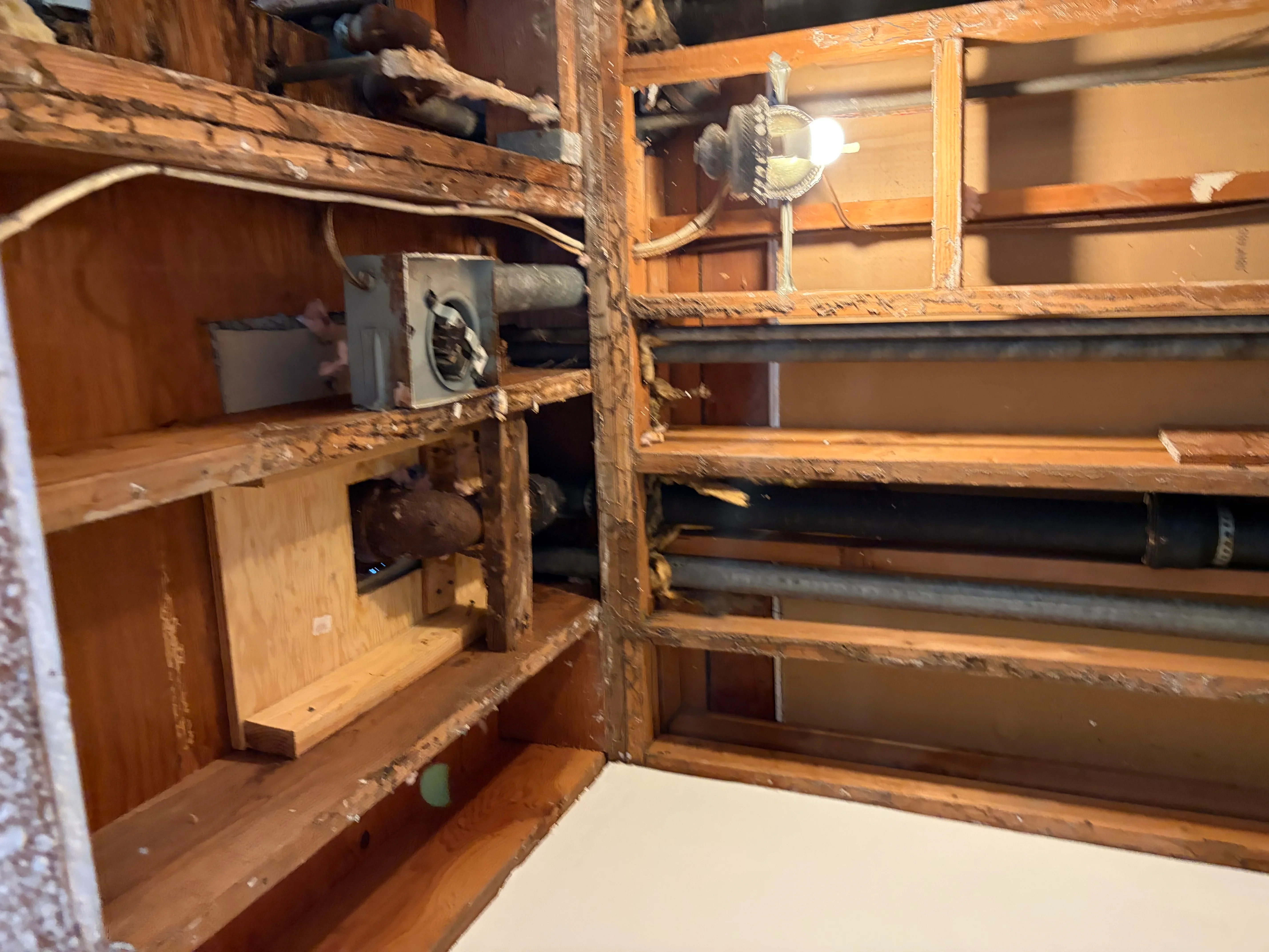 Wooden cabinet interior with brass valve, copper piping, and wooden shelves during plumbing work